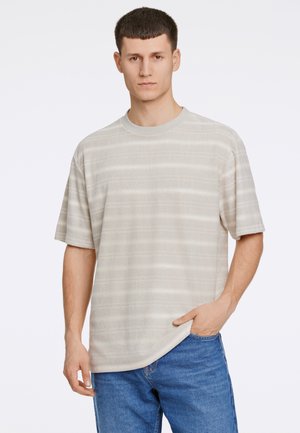 T-shirt beige à rayures, à manches courtes et col rond, fabriqué en tissu doux. Le modèle l'associe avec un jean en denim bleu.