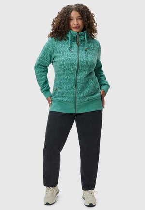 Hoodie zippé bleu sarcelle avec un motif texturé, des poignets élastiques et une capuche à cordon. Assorti avec un pantalon gris foncé et des baskets de couleur claire.