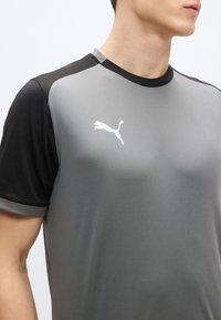 Γκρι αθλητική μπλούζα με κοντά μανίκια και μαύρες λεπτομέρειες, με στρογγυλή λαιμόκοψη και λευκό λογότυπο Puma στο στήθος. Λείο ύφασμα.