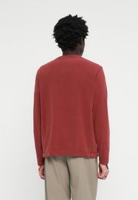 Sweatshirt rouge en tissu doux, avec col rond et manches longues, munie de poignets et d'un ourlet côtelés, présentant des détails de couture visibles.