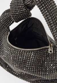 Saco preto coberto com strass metálicos, apresentando um fecho com zíper e uma alça texturizada e com nó. O interior possui um bolso com zíper.
