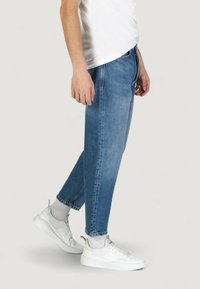 Jeans in denim azzurro chiaro con vestibilità rilassata, dotati di cinque tasche e una leggera scoloritura. Abbinati a sneaker bianche e calzini grigi.
