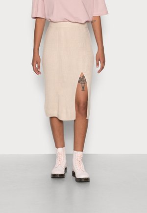 Strick-Midi-Rock in Beige mit gerippter Textur und seitlichem Schlitz; kombiniert mit hellrosa Schnürstiefeln. Einfaches und figurbetontes Design.