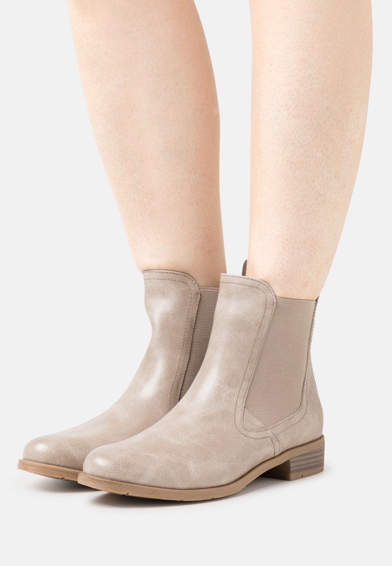 Bottes beige à la cheville avec une finition en cuir lisse, des panneaux latéraux élastiques, un bout rond et un petit talon empilé. Texture subtile et détails minimaux.