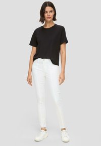 Schwarzes Baumwoll-T-Shirt mit kurzen Ärmeln, kombiniert mit weißen Slim-Fit-Jeans aus Denim mit Knopfverschluss und dezenten Seitennähten. Weiße Sneakers.