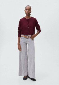 Burgunderfärgad stickad kappa med knappar, ihop med högmidjade, vida gråjeans. Svarta skor och ett beige bälte fulländar outfiten.