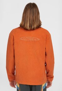 Giacca di velluto a coste arancione con maniche lunghe, orlo arrotondato e design del logo sul retro. Tessuto morbido, vestibilità casual.