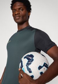 Športová košeľa v sivej a čiernej farbe s krátkymi rukávmi, ktorú drží osoba vedľa vzorovaného futbalového lopty.