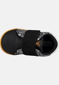 Zapato infantil negro con una parte superior de patrón en blanco y negro, acentos naranjas y una correa de velcro negra. Suela de goma con punta redonda.