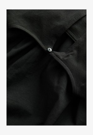 Tissu en coton noir avec une texture douce, doté d'un col arrondi et d'un bouton décoratif. Coutures lisses et bords nets sont visibles.