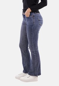 Jeans in denim blu a palazzo con tasche anteriori e posteriori, presentano una lavatura media e una leggera usura alle cuciture. Abbinati a sneakers bianche.