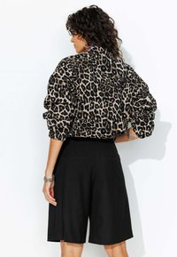Sweatshirt surdimensionné à imprimé léopard avec des manches retroussées, associé à un short noir mi-long. Tissu lisse et coupe décontractée sont mis en avant.