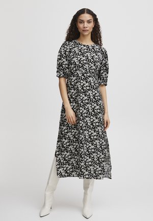 Robe noire à fleurs avec des manches bouffantes, présentant des motifs floraux légers, un col rond et une coupe fluide. Portée avec des bottes blanches jusqu'aux genoux.