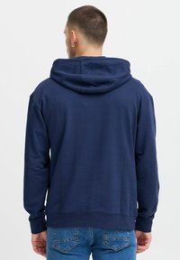 Navy blue hoodie with kangaroo pocket, drawstring hood, and ribbed cuffs. Fabric appears soft with a smooth texture. Casual fit style.