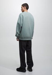 Sudadera gris claro de corte relajado, con puños acanalados y escote redondo, combinada con jeans negros de corte holgado y zapatillas negras.