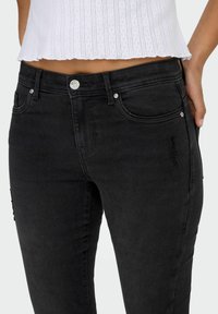 Mustad teksad, mille lõige on kitsas, sileda tekstuuriga, ees taskud ja õrnad kulumise detailid sääre piirkonnas. Hõbedased riistvara aktsendid.