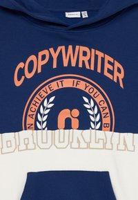Sudadera azul marino con acentos en blanco y beige, que presenta un gran texto en naranja "COPYWRITER" y "BROOKLYN" junto con un gráfico circular y un diseño de laurel.