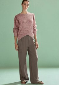 Pulover texturat de culoare roz deschis, cu guler rotund, purtat cu pantaloni lejeri de culoare taupe, prevăzuți cu buzunare laterale pentru cargo. Sandale neutre.
