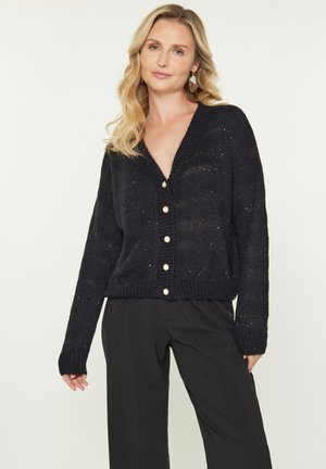 Cardigan nero lavorato a maglia con scollo a V, maniche lunghe e cinque grandi bottoni color crema sulla parte anteriore. Materiale testurizzato con una vestibilità ampia.