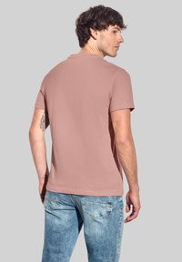 Ljusrosa t-shirt med kort ärm, tillverkad av mjukt tyg, med klassisk rund hals och slät yta, i kombination med ljusblå jeans.