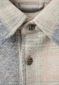 Košulja s kragnom od mekog, teksturiranog sivog materijala s suptilnim kariranim uzorkom, koja ima zatvaranje na gumb u tamnom, mat finišu.