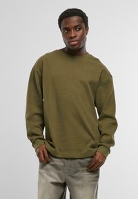 Olivza zaļa garām piedurknēm svītra ar teksturētu audumu, apaļu kakla izgriezumu un ribotām piedurknēm. Smalks logo detaļa uz krūtīm.