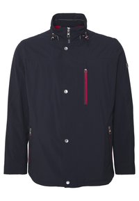 Tenký navy modrý kabát s vysokým límcem, zapínáním na patentky a zipy, a červenými akcenty na zipy a podšívce.