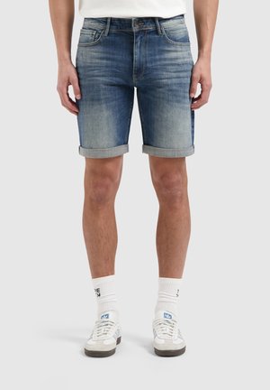 Lichte blauwe denimshorts met een rafelige zoom en opgerolde manchetten. Ontworpen met vijf zakken en een ritsluiting. Gecombineerd met witte sokken en sneakers.