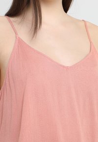 Top senza maniche di un rosa pallido, con scollatura a V. Realizzato in un tessuto leggero e texturizzato con spalline sottili. Fit casual e rilassato.
