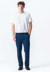 Hvid t-shirt med korte ærmer, der er parret med marineblå bukser. Bukserne har en lige pasform og knaplukning. Sorte sko fuldender outfittet.