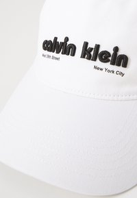 Fehér baseball sapka texturált anyagból, fekete hímzett felirattal: "calvin klein", "West 39th Street" és "New York City".