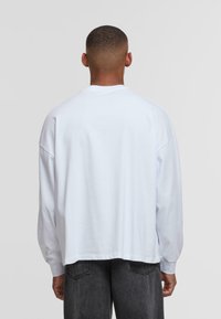 White long-sleeve shirt made of soft cotton, featuring a relaxed fit, dropped shoulders, and a straight hem. No visible patterns or accents.