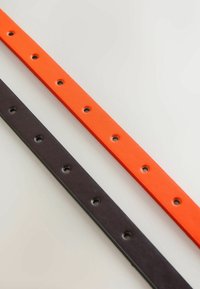 Deux ceintures en cuir, l'une orange vif et l'autre marron foncé, chacune présentant une rangée de trous uniformément espacés sur une surface claire.