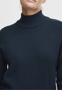 Granatowy sweter z golfem wykonany z dzianiny o prążkowanej fakturze. Charakteryzuje się wysokim kołnierzem i dopasowanym krojem, podkreślającym gładką, miękką strukturę.