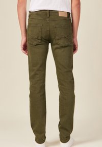 Jeans verde oliva con una vestibilità slim, dotati di due tasche posteriori e un'etichetta testurizzata in vita. Il tessuto presenta una sottile lucentezza.