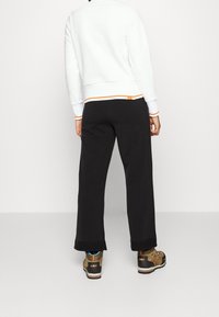 Vit texturerad sweatshirt med orange detaljer, kombinerad med svarta vida byxor och bruna vandringsskor med svarta och orangea inslag.