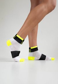 Schwarz-gelbe sportliche Knöchelsocken mit einem Mesh-Design, gestreiften Akzenten und Farbelementen im Color-Blocking mit einer strukturierten Oberfläche.