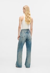 Gaiši zili augsta vidukļa platās bikses ar nodilušu izskatu, ar aizmugurējām kabatām un diegu piegriezto jostasvietu. Saskaņots ar baltu ribotu topu.