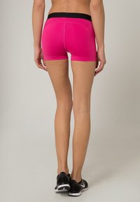 Shorts de sport roses avec une ceinture noire, offrant une coupe ajustée et une texture lisse, adaptés à une tenue active.