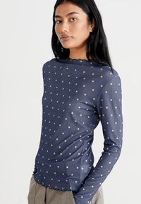 Maglietta a maniche lunghe color navy con piccoli pois gialli, tessuto a coste, scollatura ondulata e design aderente.