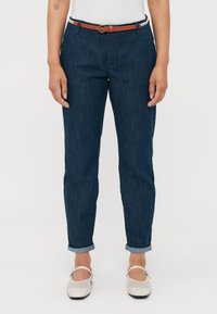 Tmavě modré džínové kalhoty s uvolněným střihem, srolovanými manžetami a hnědým koženým opaskem se zaoblenou sponou.