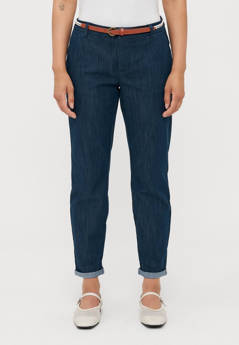 Tmavě modré džínové kalhoty s uvolněným střihem, srolovanými manžetami a hnědým koženým opaskem se zaoblenou sponou.