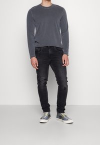 Grå långärmad skjorta, svarta slim-fit jeans med slitna knän och blå sneakers med gröna snören och vita sulor.
