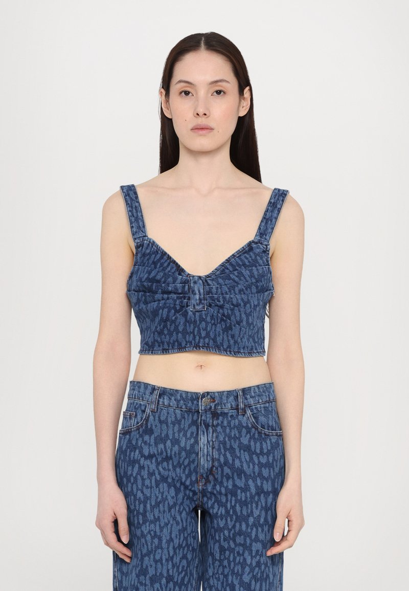 Κομμένο τζιν τοπ με φαρδιές τιράντες, V-λαιμόκοψη και λεπτομέρεια με κουμπιά μπροστά. Σε σχέδιο με αποχρώσεις του μπλε, συνδυασμένο με ταιριαστά τζιν.