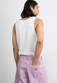 White sleeveless tank top paired with light pink cargo shorts, featuring two back pockets, one with a Carhartt logo.