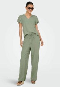 Ljust grön, kortärmad topp med V-halsringning, tillsammans med matchande vida byxor med dragsko i midjan. Bärs med bruna kilklackssandaler.