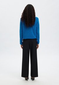 Modra pletena majica združena s črnimi širokimi hlačami, pogled od zadaj. Gladek tekstura in preprost dizajn z dolgimi rokavi.