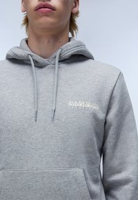 Sweatshirt gris en matériau doux avec une poche kangourou, arborant un logo blanc discret sur la poitrine et des cordons de serrage réglables sur la capuche.