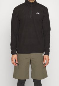 Pullover in pile nero con zip a quarti e colletto alto. Abbinate a pantaloni corti verde oliva con tasche con zip.