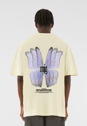 Yellow cotton t-shirt featuring a large blue butterfly graphic on the back, with black text below detailing the theme "METAMORPHOSE."